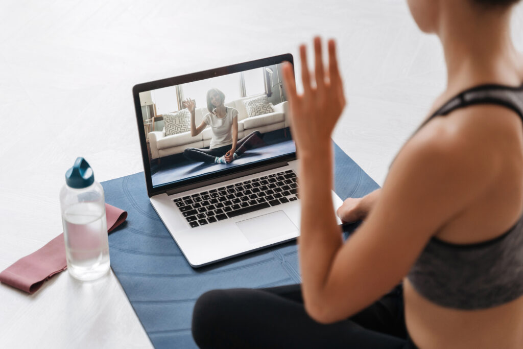Eine motivierte Frau sitzt im Wohnzimmer vor ihrem Laptop und macht mit Begeisterung einen Online-Fitnesskurs bei Love Your Body.